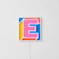 Néon LED en forme de lettre E rose sur fond multicolore bleu jaune orange dans cadre carré sur mur blanc